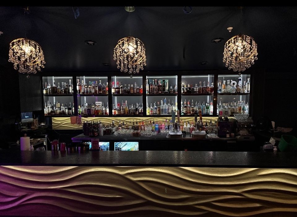 The bar in the L wing at The Pink Elephant, chandeliers over a lit back bar